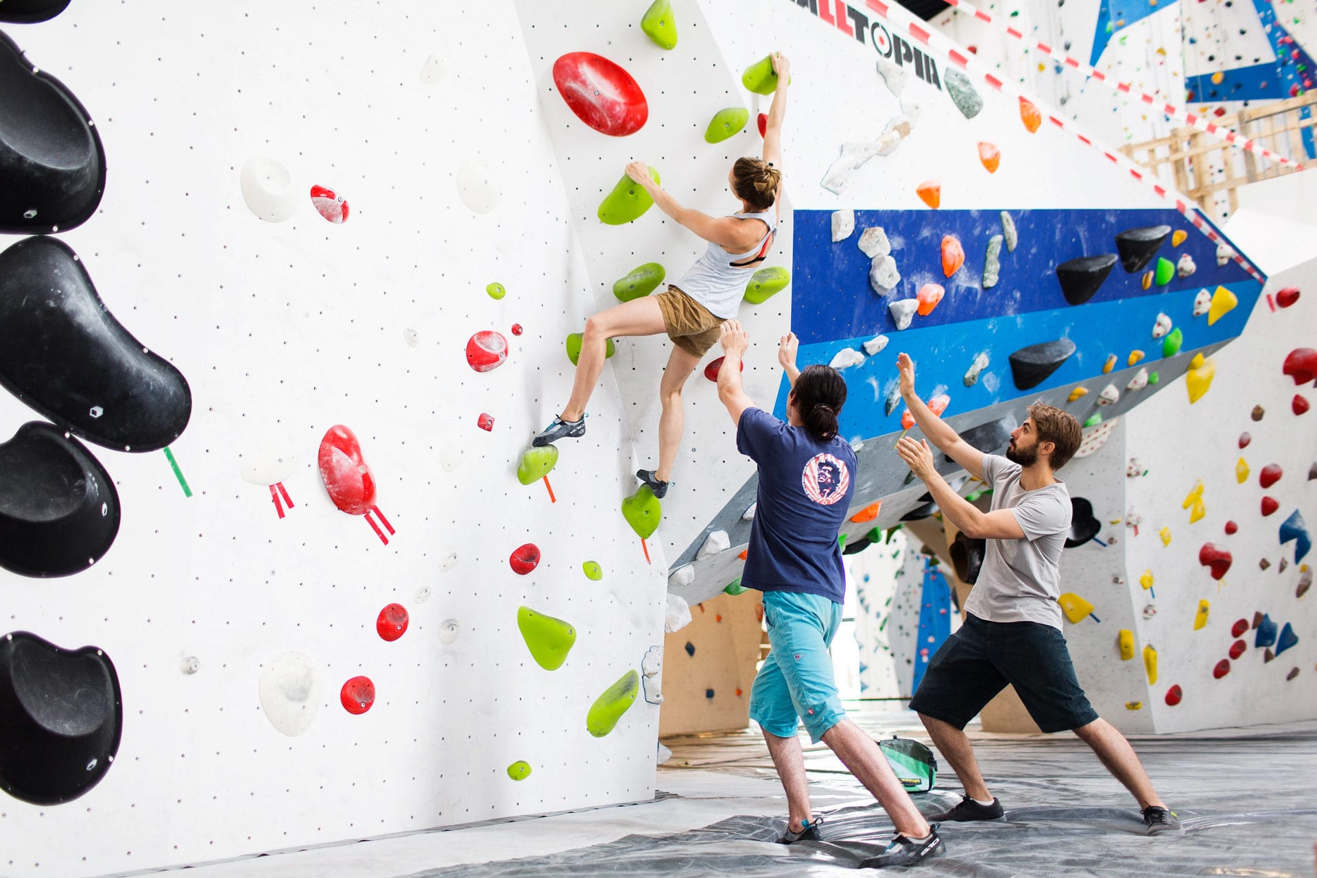 Person an Boulderwand und 2 Personen daneben