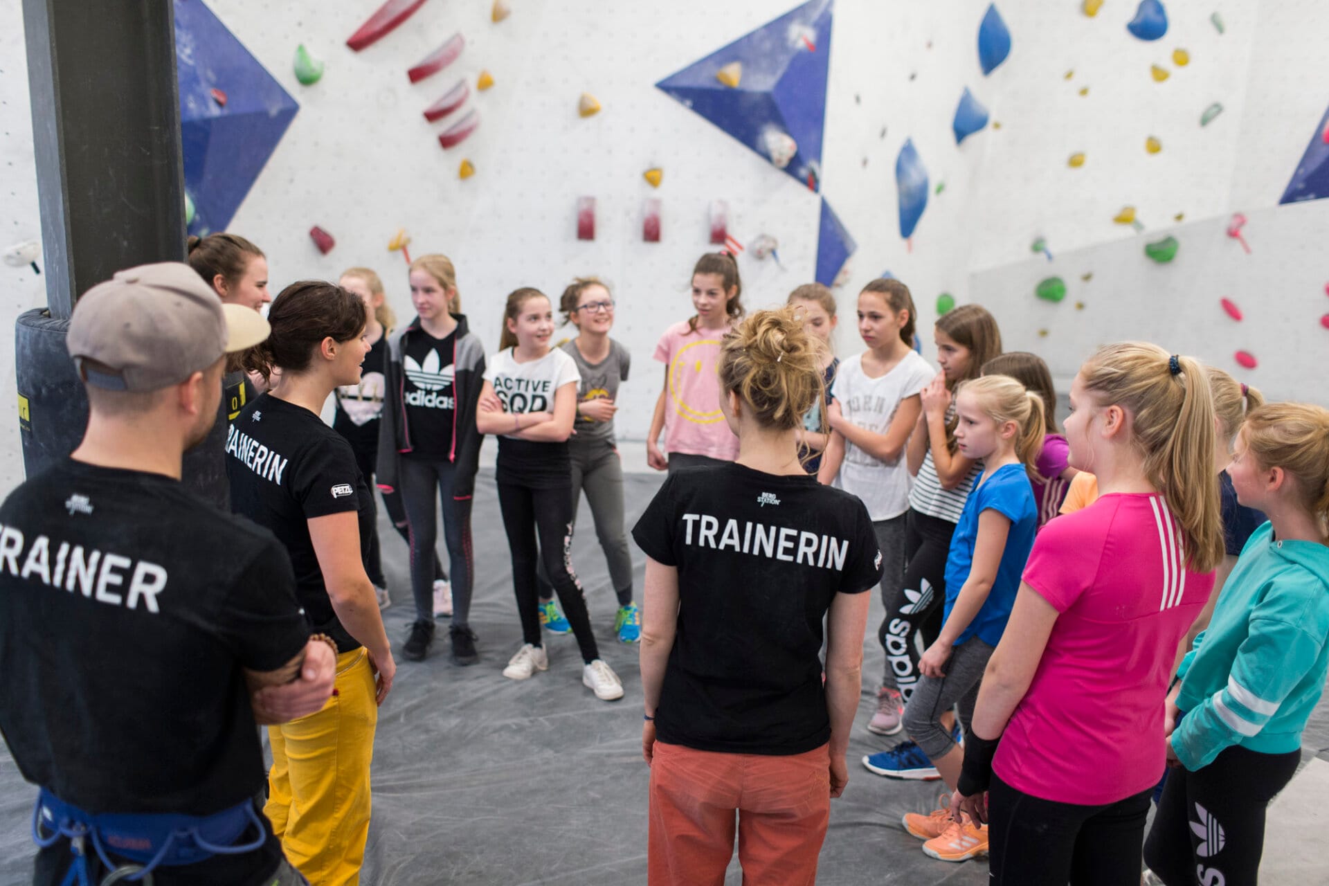 Mehrere Trainer*innen und Kinder vor einer Boulderwand