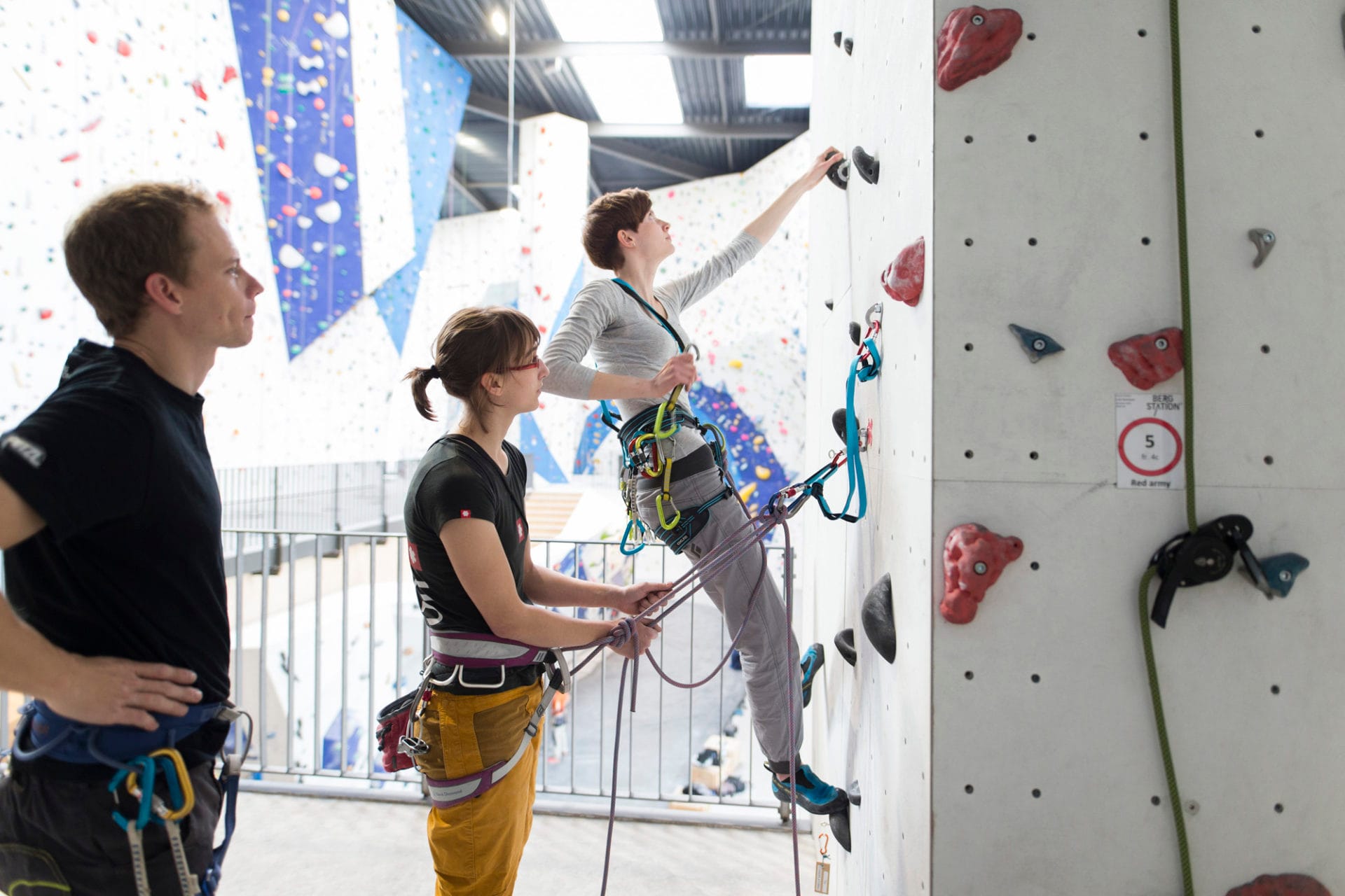 Kletterin an Kletterwand wird gesichert unter Aufsicht eines TRainers