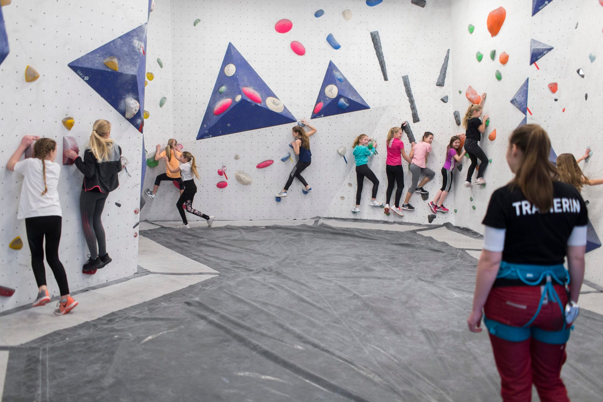 Kinder an Boulderwand unter Aufsicht einer Trainerin