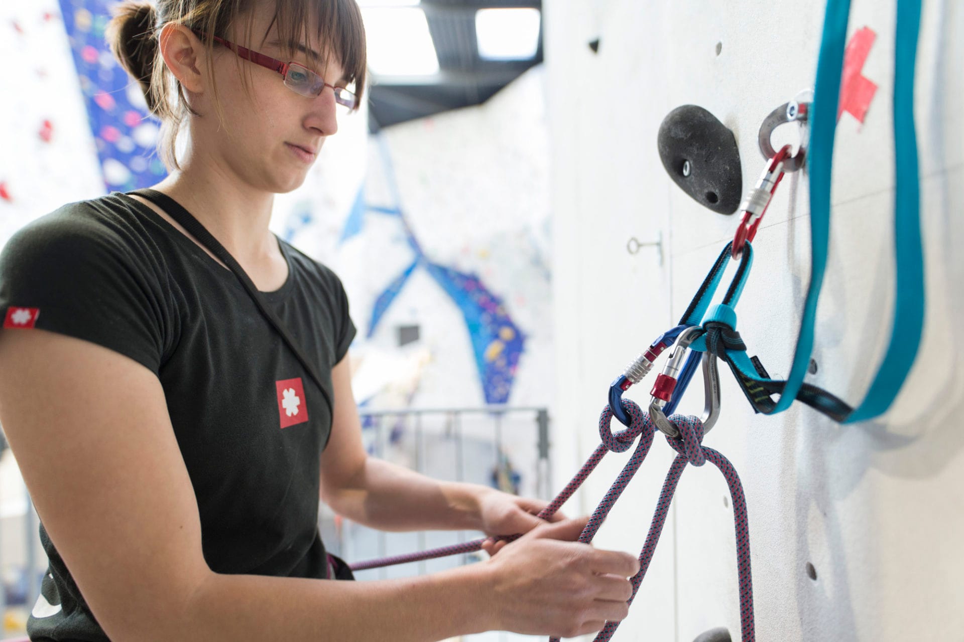 Frau macht Knoten an Karrabiner an Kletterwand